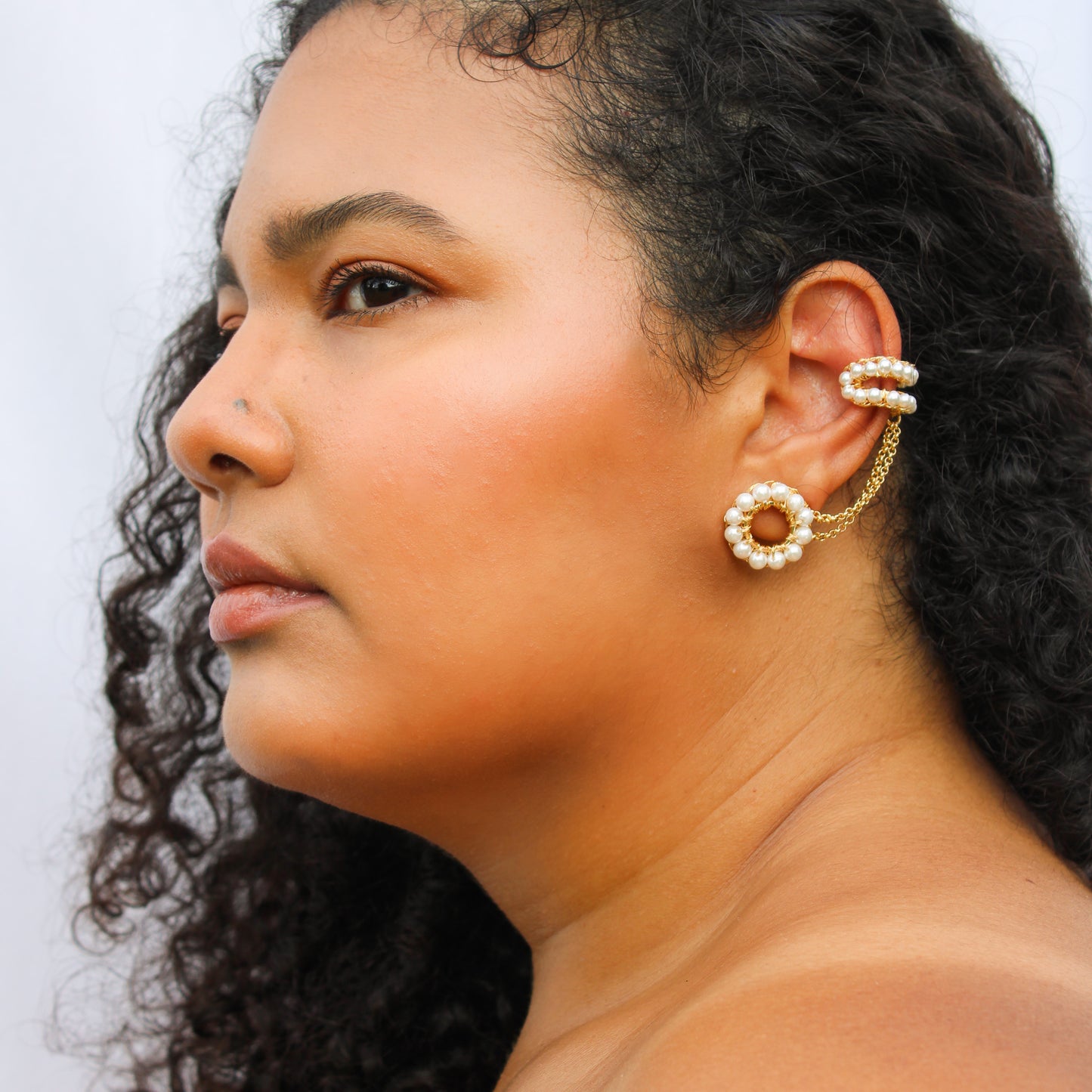 double-ring earring design, handcrafted with pearls woven onto a gold-plated frame. A delicate chain connects the two cuffs on one side.  Lightweight earrings