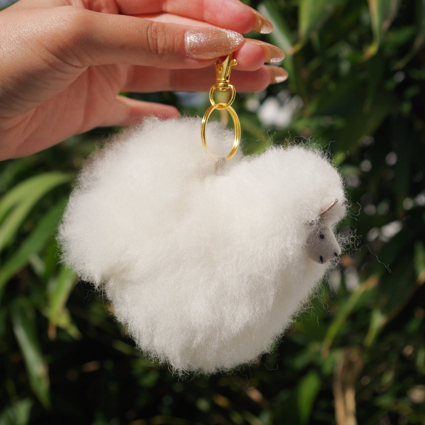 Llama plushie pom pom keychain. Pom Pom size 3” in approx. Made with 100% alpaca wool. Made by Bolivian and Peruvian artisans. Colors Available: pink, white, beige, purple. Adult or children gift side view