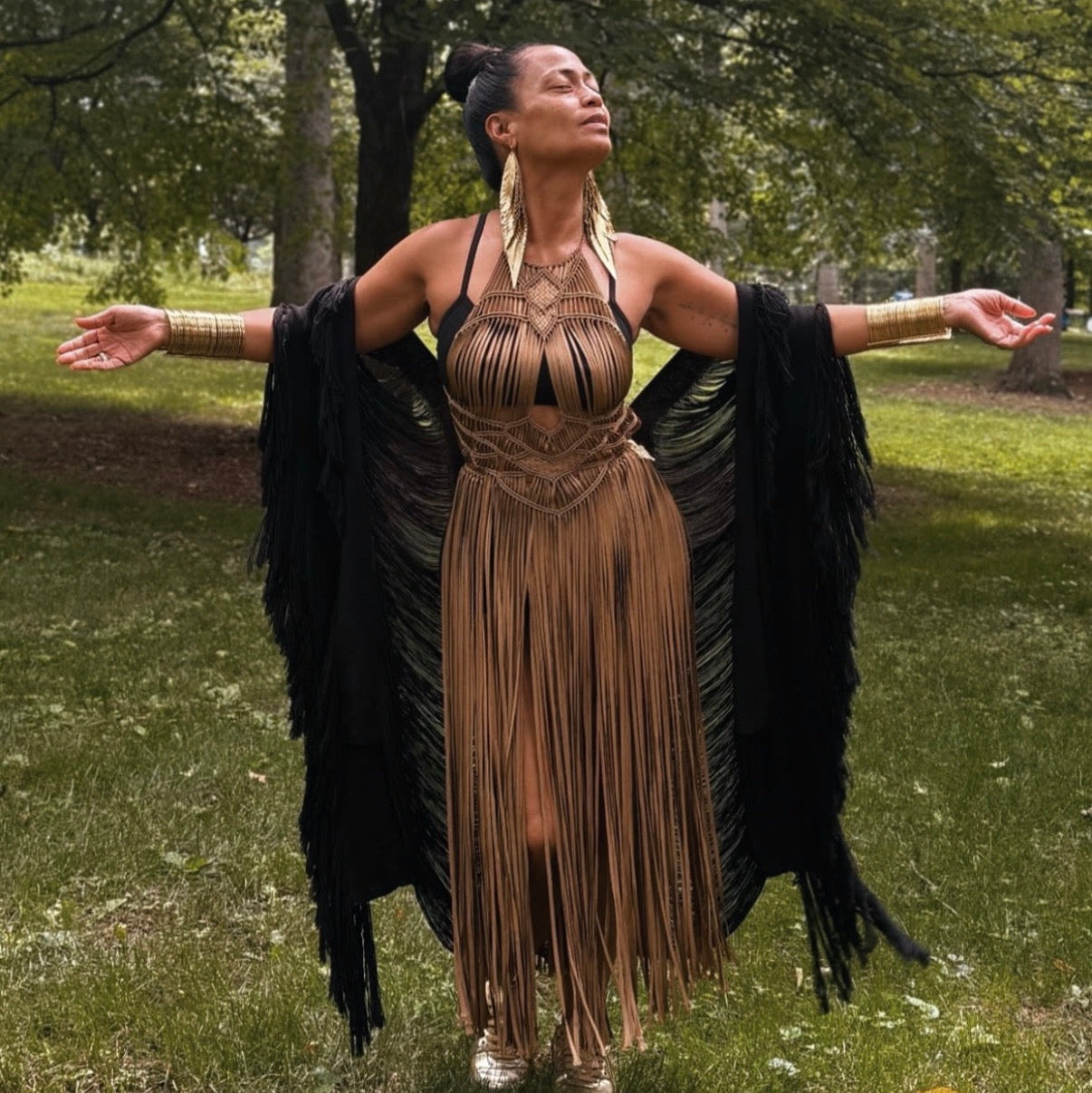 Woman in a bronze luna fringe dress and black shawl standing in a park.