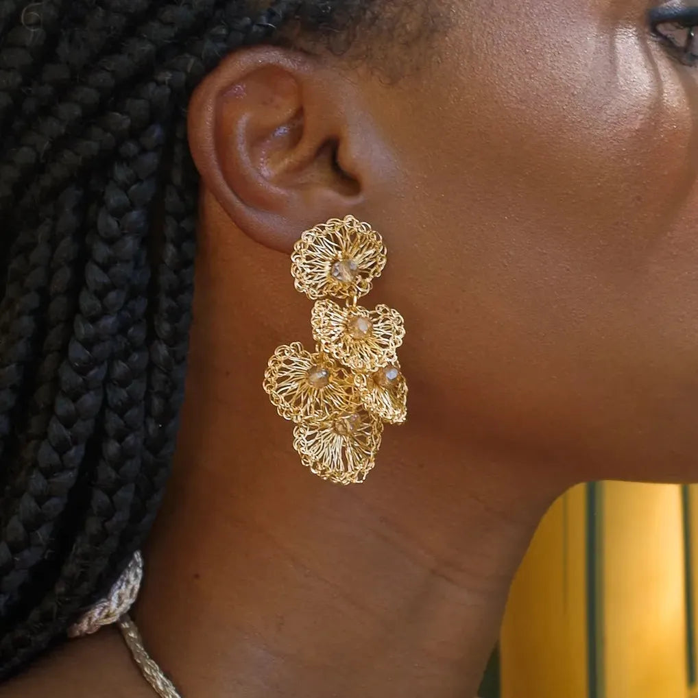 Gold shell like crochet wired earrings worn by a person with braided hair.