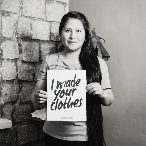 Artisan holding a sign that reads 'I made your clothes' against a brick wall.