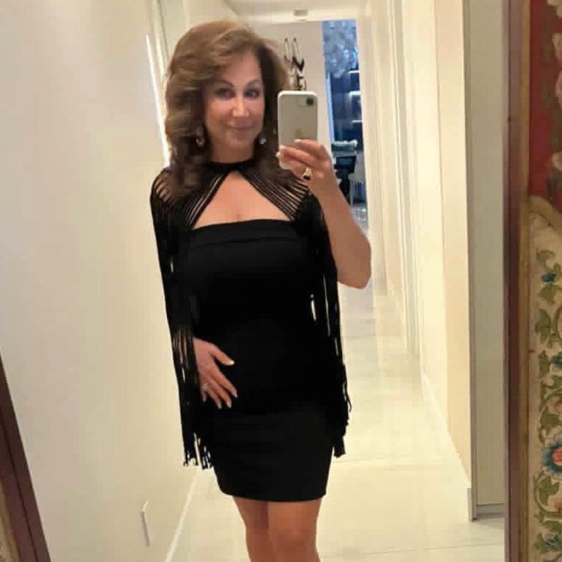 Woman taking a mirror selfie wearing a black cape with fringe details.
