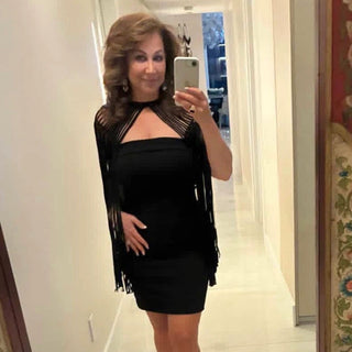 Woman taking a mirror selfie wearing a black cape with fringe details.