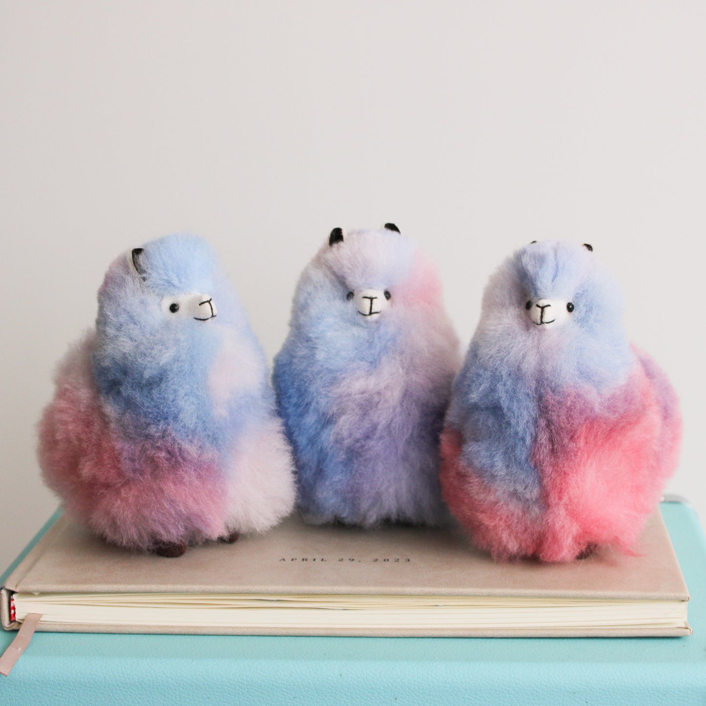 Three fluffy, gradient-colored llamas with pink lilac and light blue colors. Alpaca fur llama plushies.