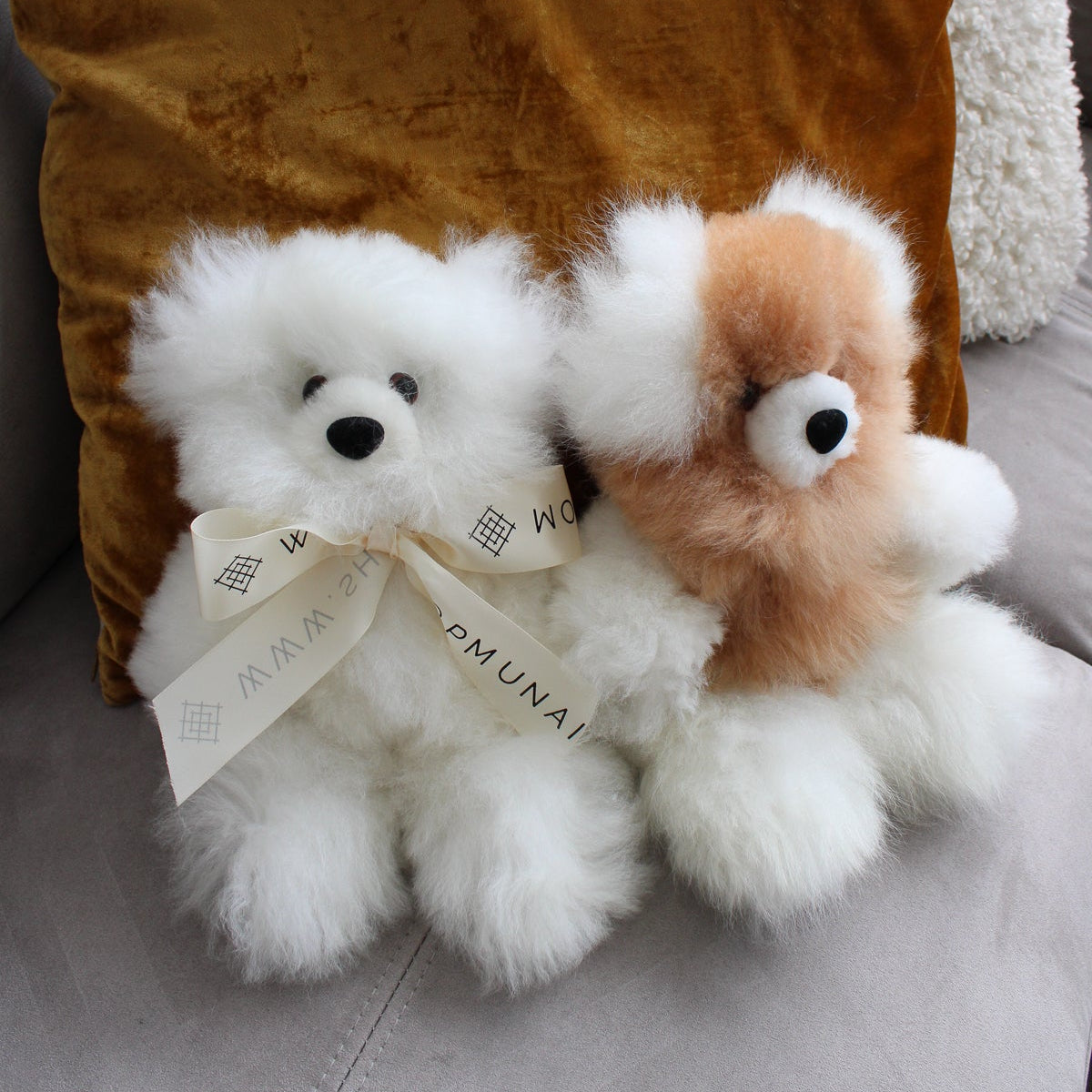 Two spotted two-color teddy bears with ribbons sitting on a couch